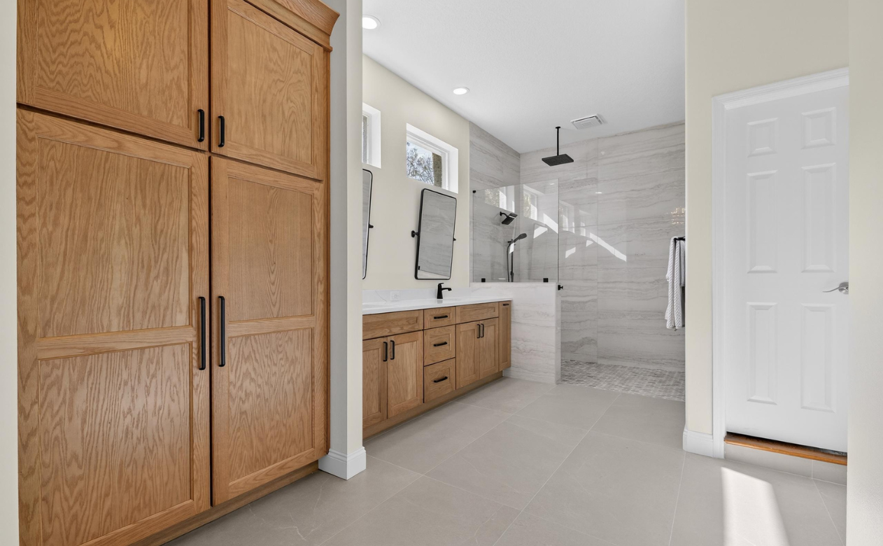 Luxurious bathroom remodel with gray tile flooring, matching vanity and cabinetry, walk-in shower, and black fixtures in Westchase, FL