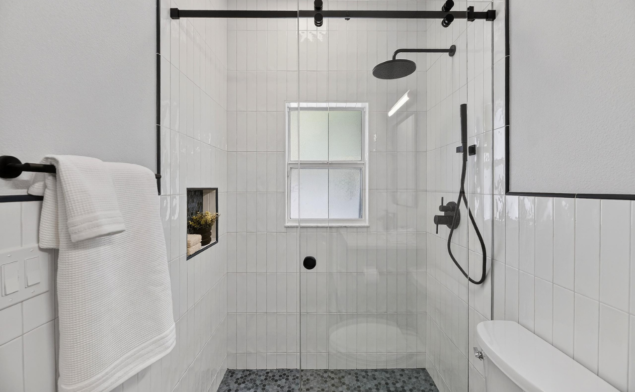 Bathroom renovation with white wall tile, niche, black hardware, sliding glass doors, and mosaic tile flooring from Hanover Floors